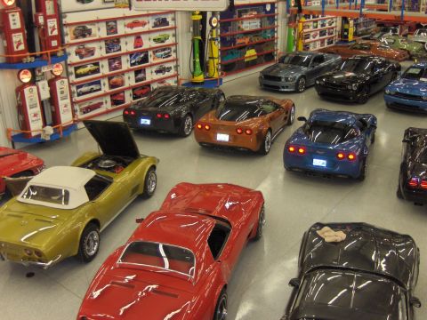1979 Chevrolet Camaro - A variety of toy cars are displayed in a showroom, some with hoods open, alongside vintage gas pumps and shelves of car models.