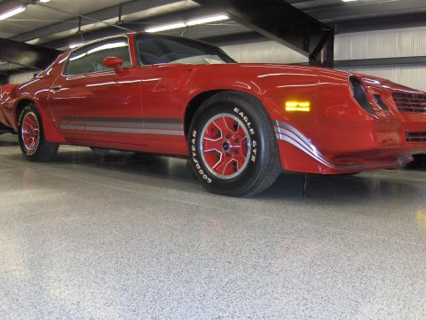1979 Chevrolet Camaro - A red 1979 Chevrolet Camaro is shown with silver racing stripes along its side and distinctive red wheels.