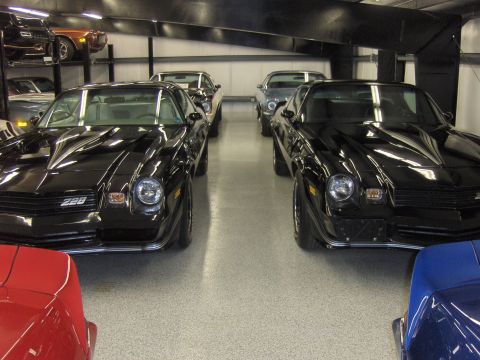 1979 Chevrolet Camaro - Two black Chevrolet Camaros are parked side-by-side in a garage, with other vehicles visible in the background.