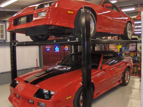 1979 Chevrolet Camaro - Two red Chevrolet Camaros are stored on a two-post car lift in a garage.