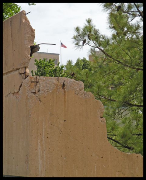 1998 Subaru Legacy - A damaged concrete structure stands against a backdrop of trees and an American flag.