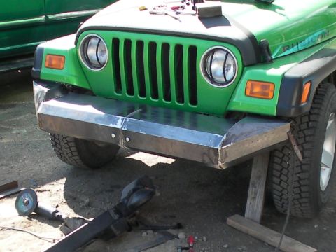 1987 Suzuki Samurai - Front view of a green Jeep Wrangler a custom metal bumper and its iconic vertical grille, with tools visible nearby.