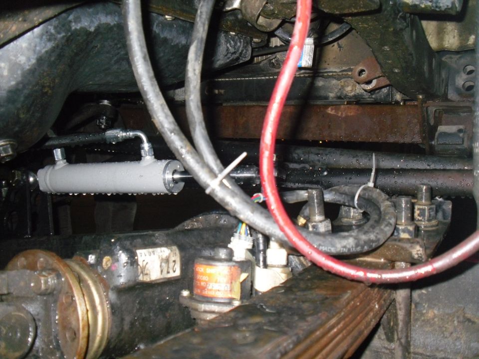 Hydraulic cylinder mounted near suspension components with visible part numbers