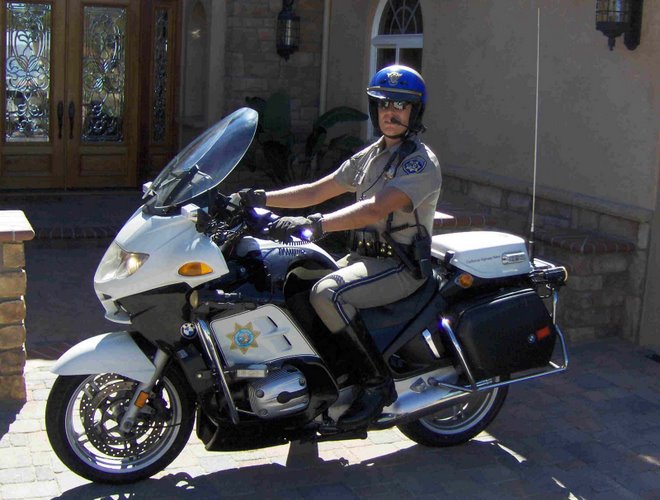 White police motorcycle with a rider in uniform, parked in front of a house