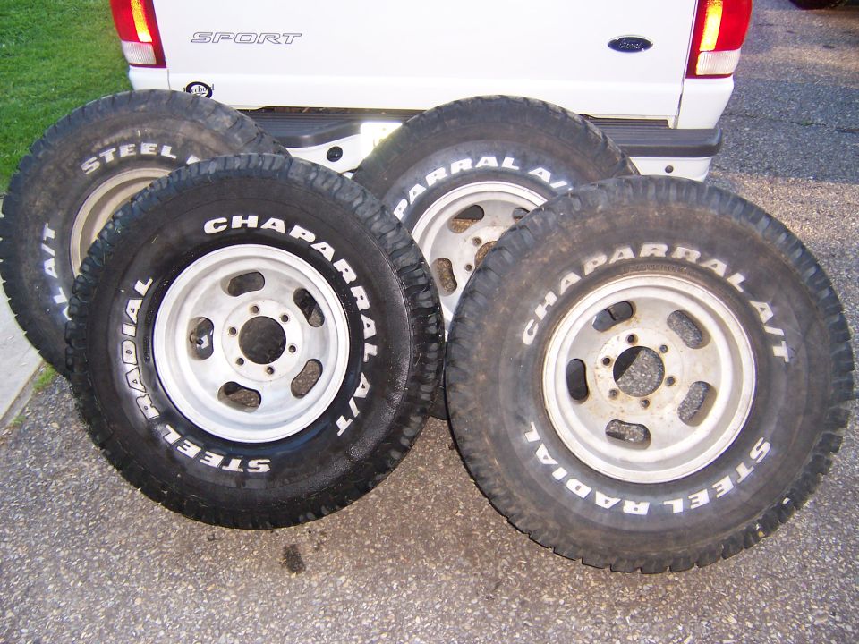 four Chaparral A/T steel radial tires on aluminum wheels stacked in front of a white pickup truck bed