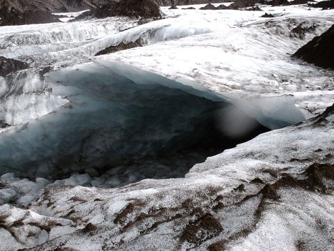 1996 Ford Bronco - Entrance to a glacial ice cave, showing deep blue ice formations and rocky debris.