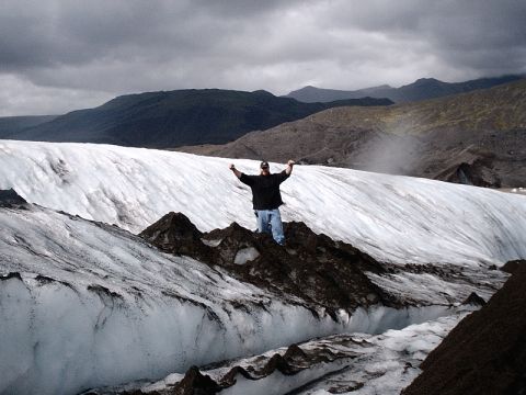 1996 Ford Bronco - A person stands triumphantly on a rocky outcrop on a vast glacier under a cloudy sky.