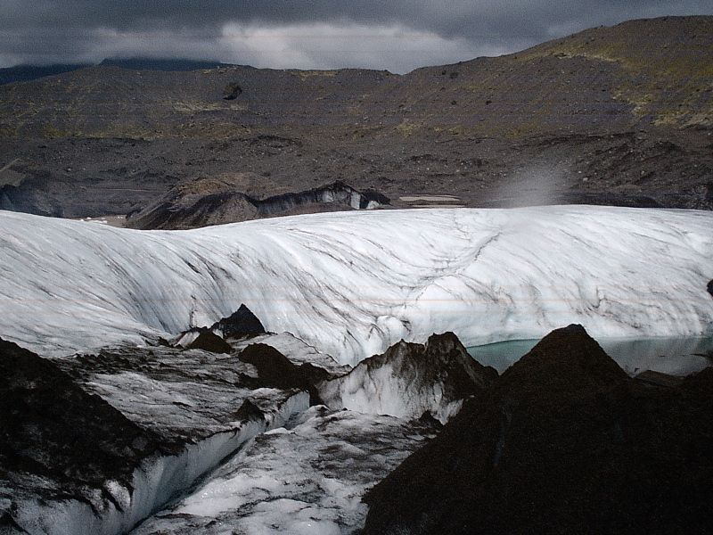 Dirty glacier ice between dark rocky ridges under overcast sky