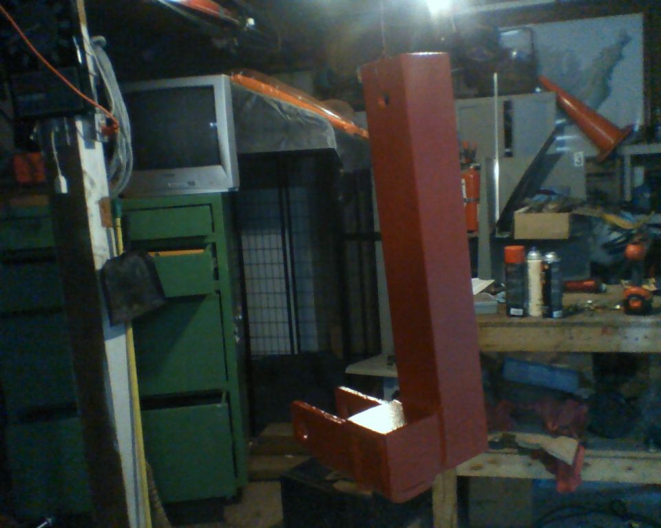 Red metal part with a box-like end, hanging in a cluttered garage