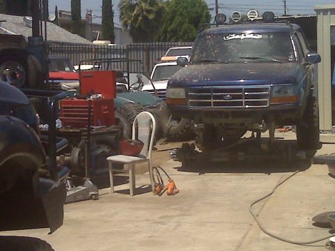 1987 Ford Bronco - Blue Ford Bronco undergoing repairs, lifted for work on suspension and drivetrain components.