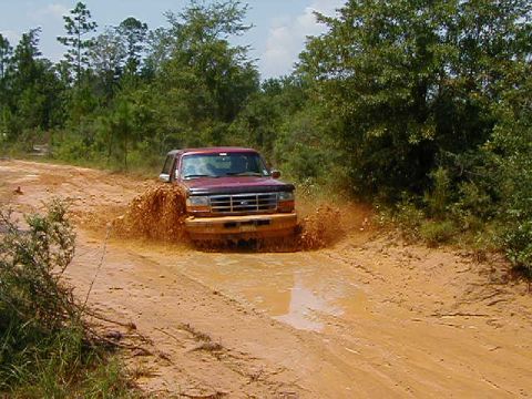 1990 Ford Bronco - 1990 Ford Bronco navigating a challenging muddy off-road path.