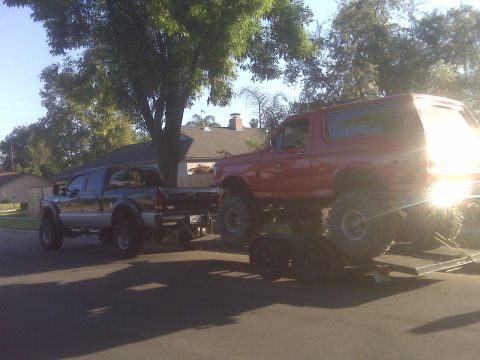 1987 Ford Bronco - A red 1987 Ford Bronco is transported on a trailer towed by a pickup truck.