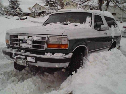 1996 Ford Bronco - This two-tone Ford Bronco is partially buried in a snowdrift, with only its front grille and headlights visible.