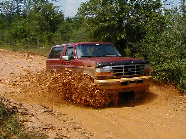 Red SUV with a black grille guard driving through mud, front view