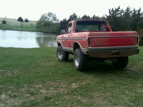 1987 Ford Bronco - This red Ford Bronco is parked near a body of water with trees in the background.