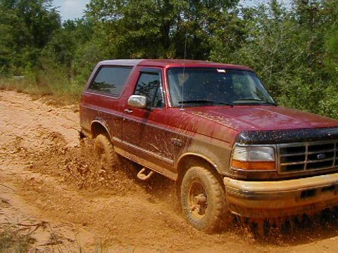 1990 Ford Bronco - Red Ford Bronco navigates a muddy trail, appearing to be a 1992 model.