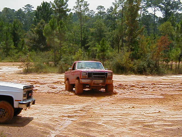Red pickup truck stuck in mud, white pickup truck to the left
