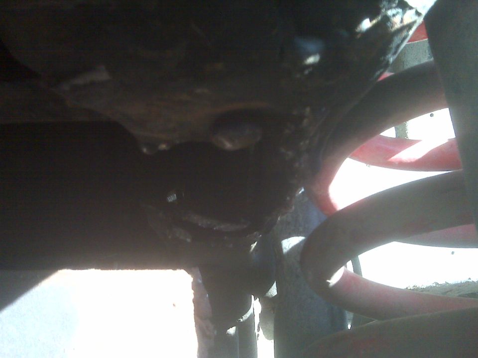 Dark underbody close-up of a red coil spring and grimy axle under a truck