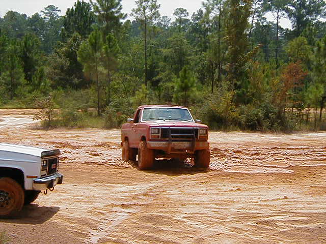 Red pickup truck with a brush guard stuck in mud, white pickup truck to the left
