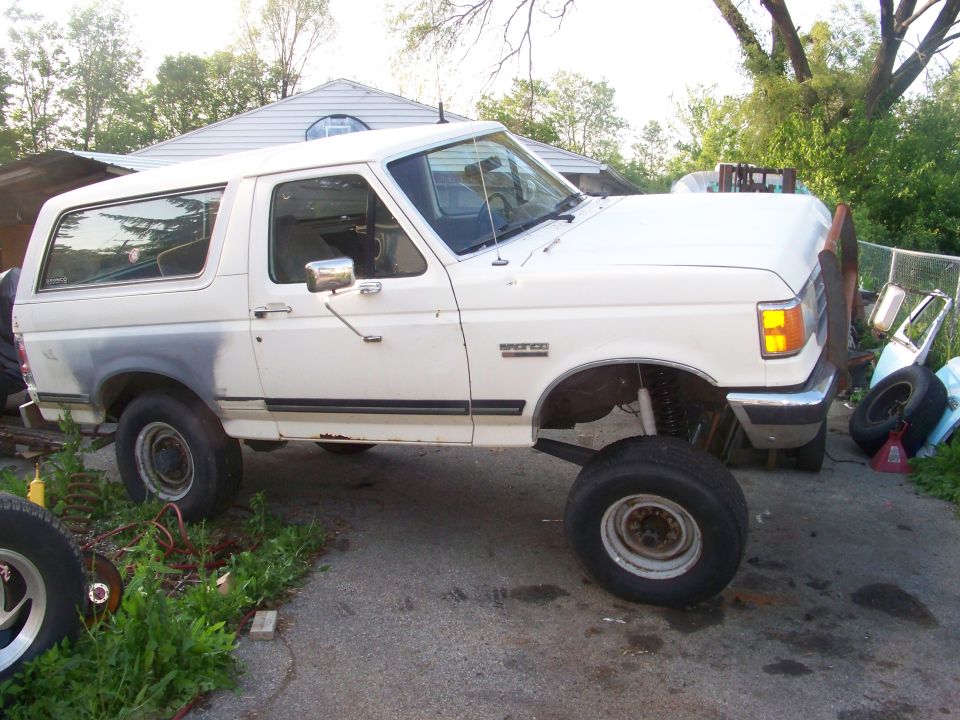 White Ford Bronco with lifted suspension and large tires parked outside a house