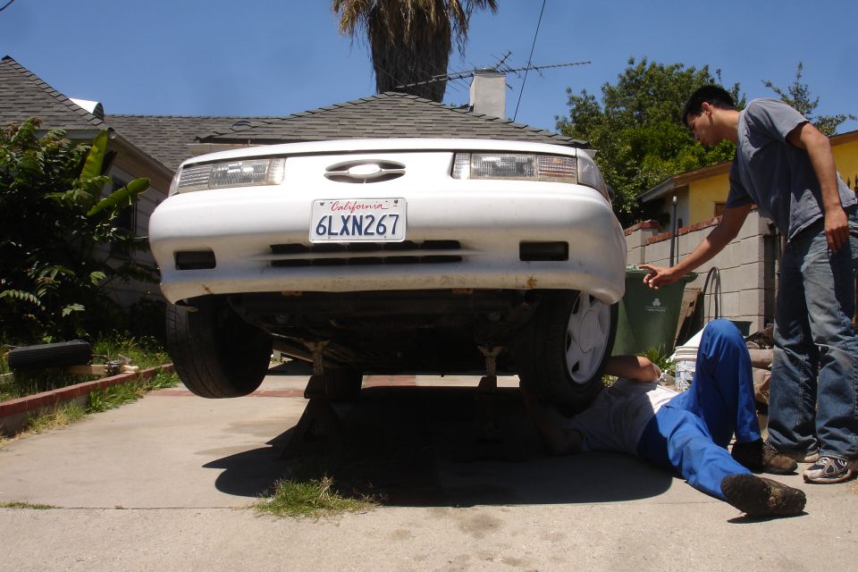 White 1992 Ford Taurus on jack stands with two people working underneath