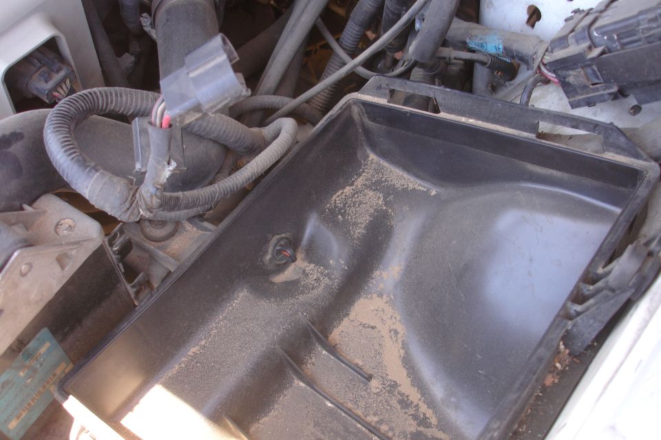 Empty dirty under-hood battery tray with surrounding wiring and connectors