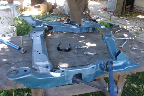 1992 Ford Taurus - A disassembled car subframe rests on a weathered wooden surface, surrounded by tools and a pair of sunglasses.