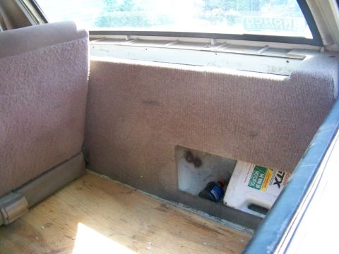 1989 Ford Bronco - Interior cargo/cargo-bin area behind a folded rear seat, with a carpeted access panel opening to oil bottles below.