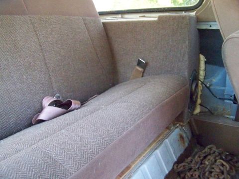 1989 Ford Bronco - The interior of a vehicle shows a rear seat with a pair of pink shoes and exposed wiring on the right side.