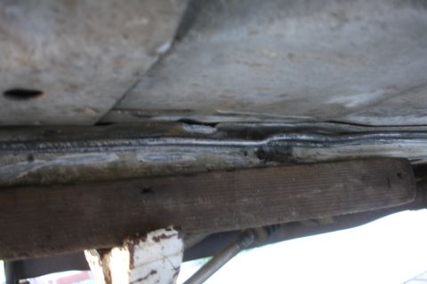 1992 Ford Taurus - Underbody view of a vehicle, supported by a wooden block, with visible rust and damage.