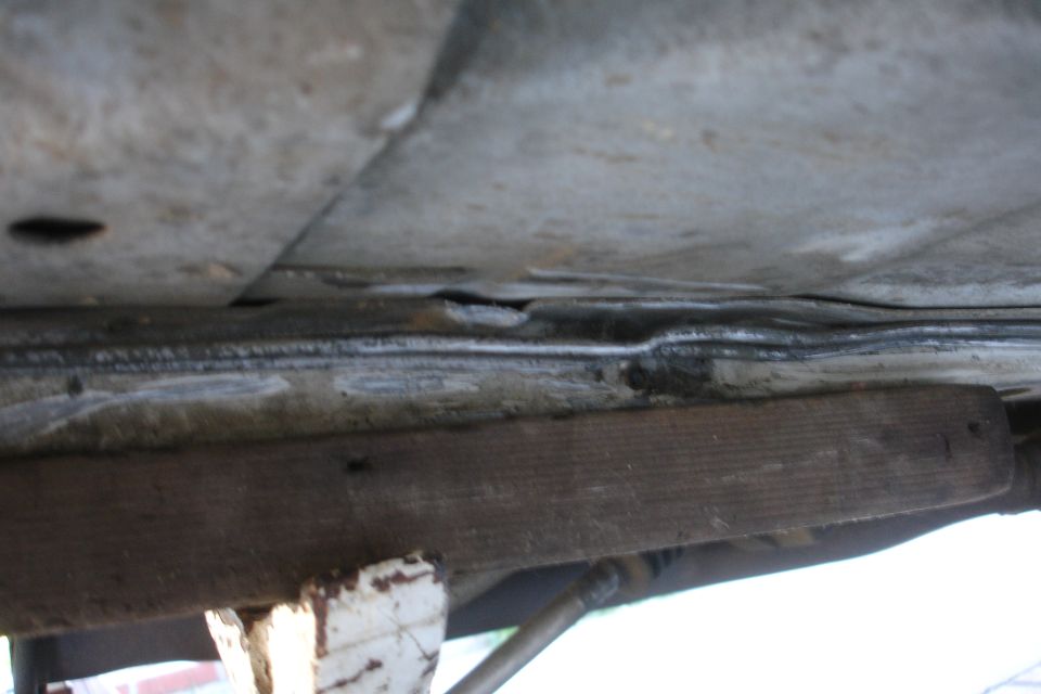 Close-up of car's underbody showing rust and a wooden block supporting it