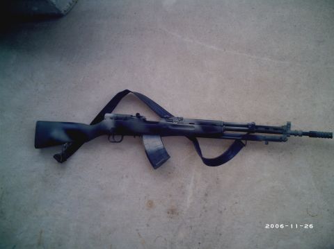 1989 Ford Bronco - An SKS rifle with a camouflage paint scheme and a sling is displayed on a concrete surface. The image also contains a SuperMotors watermark…