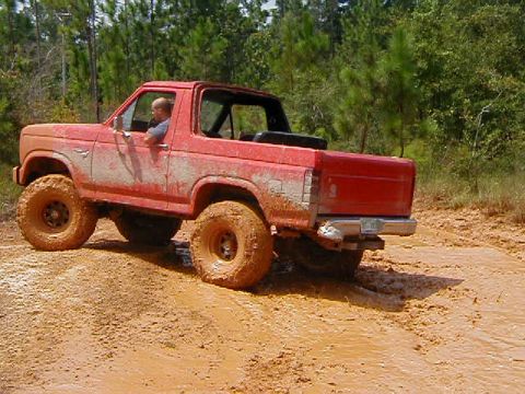 1990 Ford Bronco - This red Ford Bronco is navigating a muddy trail with a driver behind the wheel.