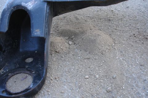 1992 Ford Taurus - A close-up view of a black metal automotive part resting on a dirt surface.