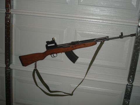 1989 Ford Bronco - An SKS rifle equipped with a red dot sight and a green sling is displayed against a white garage door.