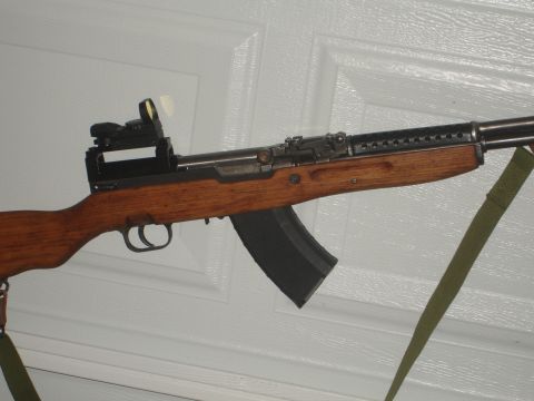 1989 Ford Bronco - A rifle with a wooden stock and a mounted red dot sight is shown against a white background.