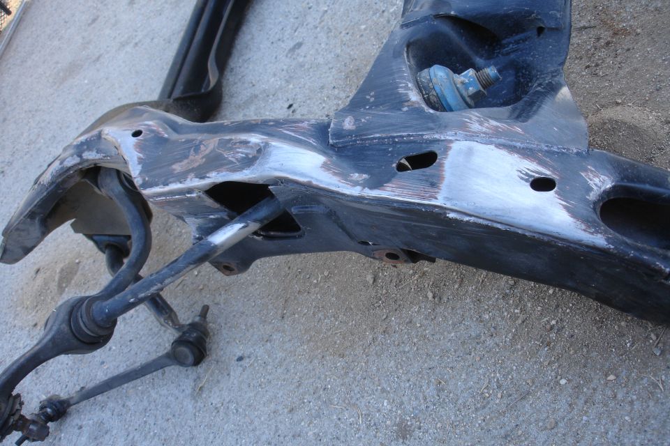 Black metal subframe assembly with suspension components attached, resting on a concrete surface