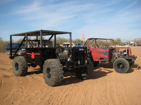 1996 Ford Bronco - Two heavily modified off-road vehicles with exposed engines sit side-by-side in a desert landscape.