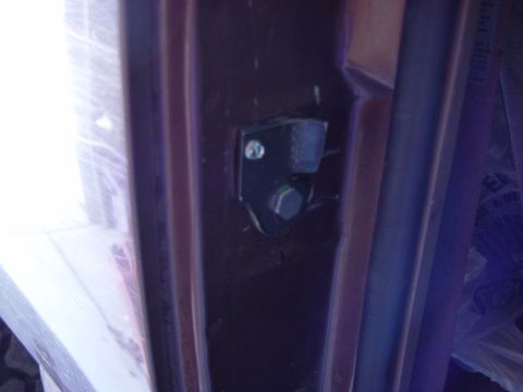 1993 Ford Bronco - Dim close-up of a door striker area on a brown truck's B-pillar, showing a black latch striker bracket held by a hex bolt and screw against…