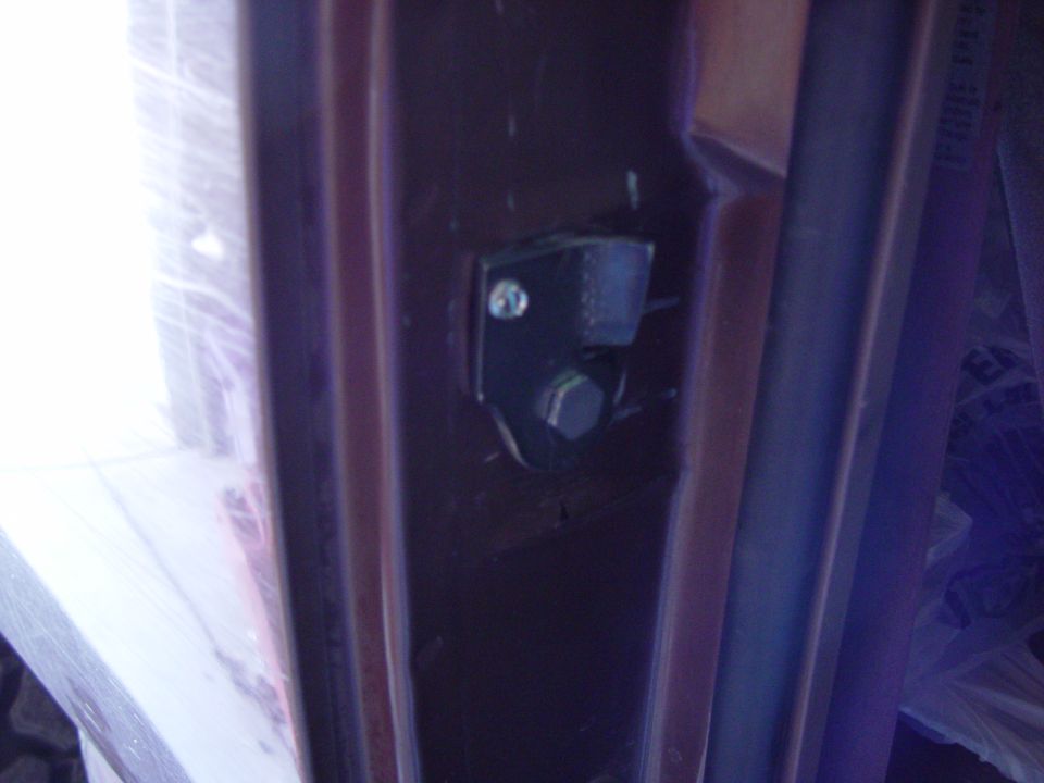 Dark close-up of bolted door striker bracket on brown truck B-pillar jamb