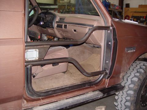 1993 Ford Bronco - Brown Ford Bronco interior with a fabricated tube door, tan dash and cloth seats, Bronco badge visible.