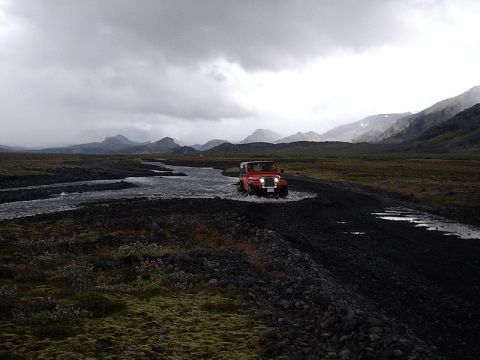 1996 Ford Bronco - Red Jeep Wrangler navigates a river crossing in a remote, mountainous terrain.
