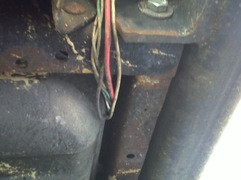 1986 Ford Bronco - Close-up view of exposed wiring and rusted metal components on a vehicle's undercarriage.