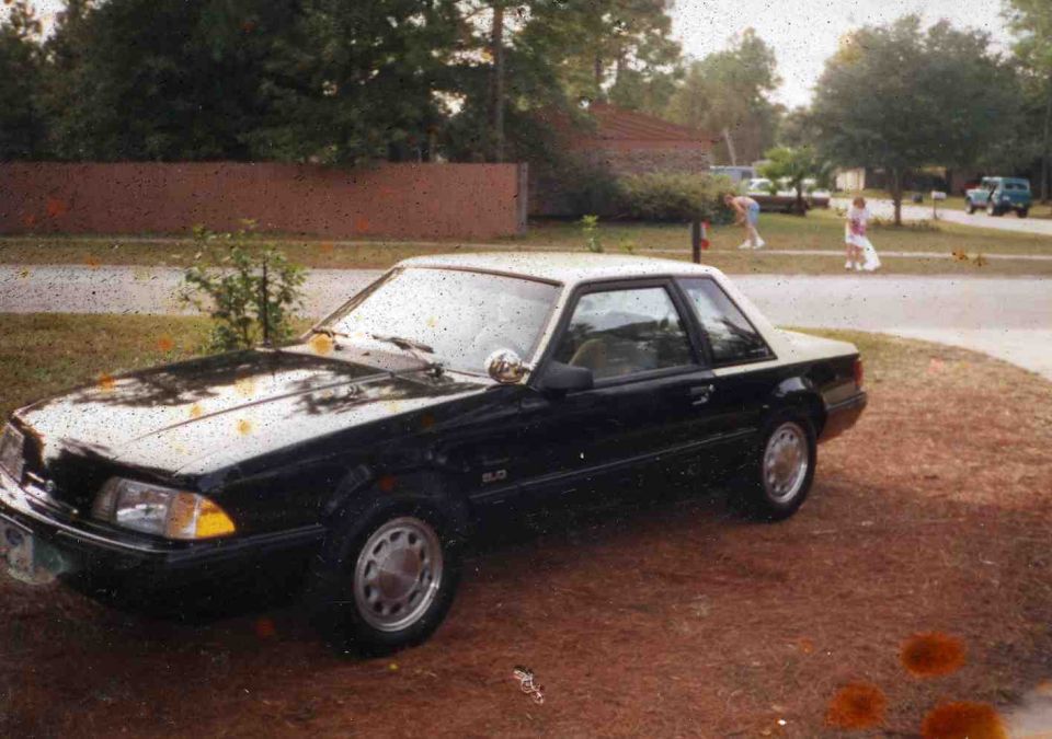Black Ford Mustang 5.0 LX notchback coupe parked in a yard