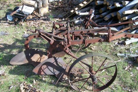 2000 Chevrolet Tahoe - An old, weathered farm plow rests outdoors, surrounded by grass and logs.