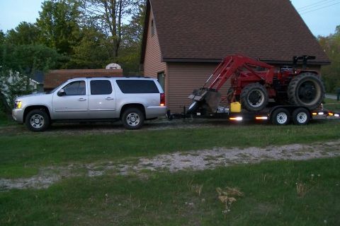 2000 Chevrolet Tahoe - A silver SUV tows a red tractor on a trailer in front of a house.