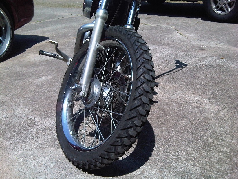 Motorcycle front wheel with knobby tire on chrome spoke rim and disc brake, on concrete