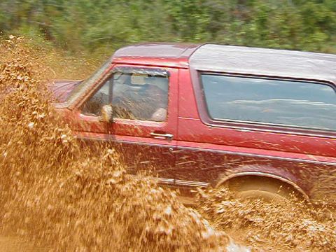 1990 Ford Bronco - This 1990 Ford Bronco is navigating a muddy off-road trail, kicking up a large spray.