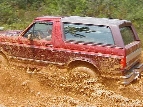 1990 Ford Bronco - This red Ford Bronco is deep in the mud, with its tires churning up the thick, wet earth.