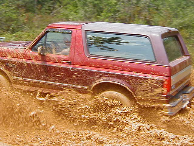 Red Ford Bronco stuck in mud, driver visible inside